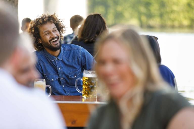 A man with a blue shirt is sitting and laughing in a beer garten in Munich.
